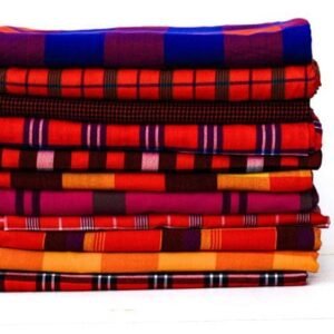 A neatly folded stack of colorful, plaid African shuka fabrics, featuring traditional patterns in red, blue, and orange, ready to be used for artisan crafts.